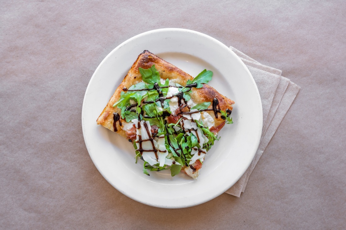 Action Pie slice topped with arugula, shaved parmesan, and balsamic glaze